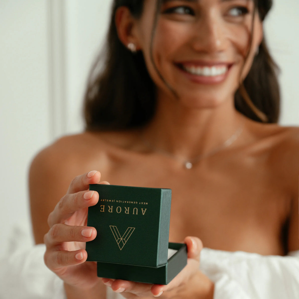 Lachende vrouw houdt een donkergroen sieradendoosje van Aurore Jewelry vast, met gouden logo en luxe afwerking.