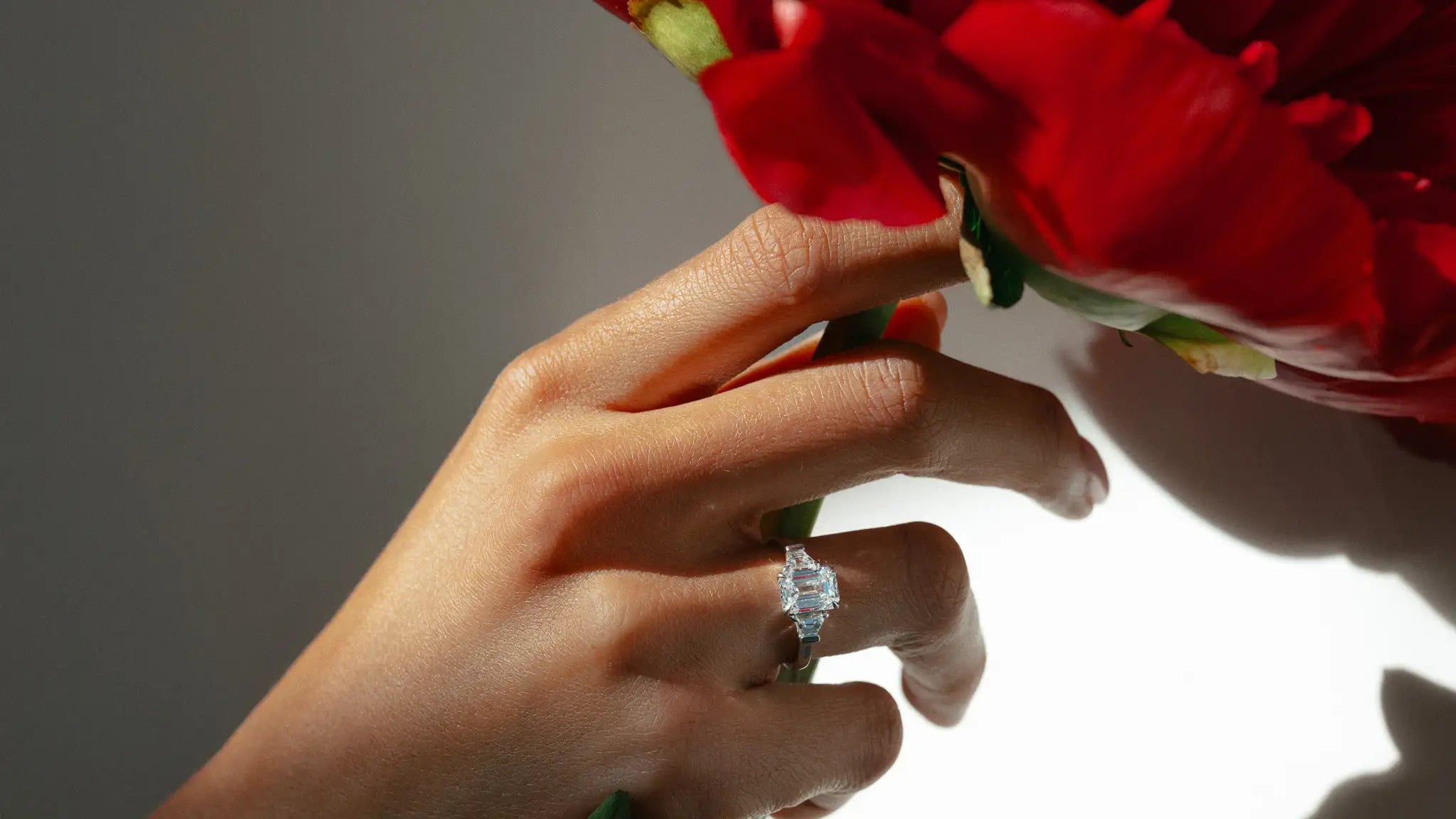 Hand met bloem en 18 karaat witgouden 3-stenen ring met 1,40 ct lab grown diamant.